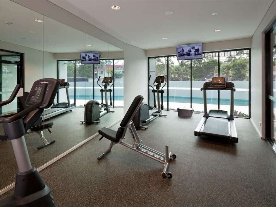 A modern gym with cardio machines, weightlifting equipment, and large windows offering a view of the outdoors.