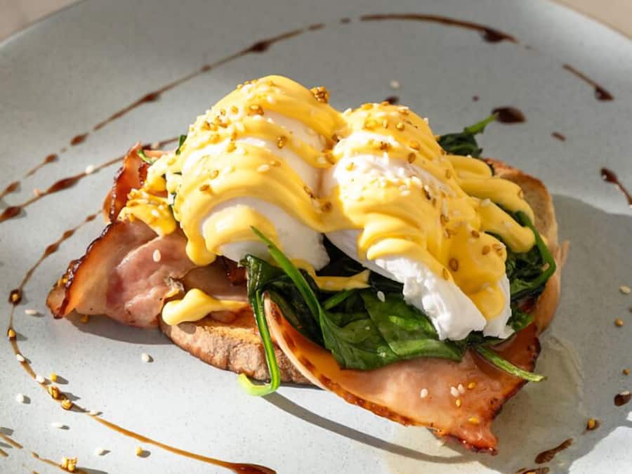 Un plato con un desayuno, posiblemente huevos Benedict, salsa y decoración.