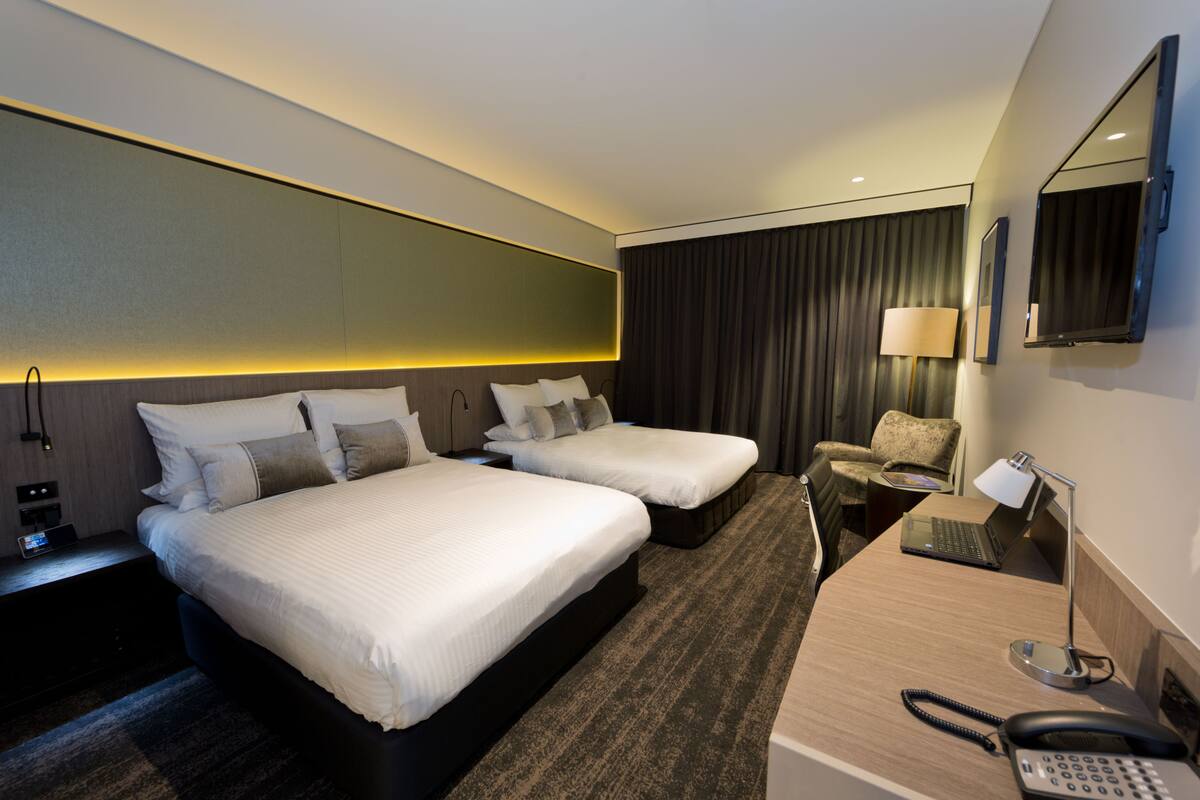 A hotel room with two beds, a desk with a laptop, a phone, and a chair.