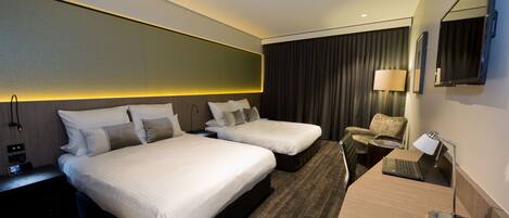 A hotel room with two beds, a desk with a laptop, a phone, and a chair.