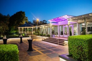 A well-lit outdoor area with a covered seating area, steps leading to a building, and neatly trimmed hedges. - The Glen Hotel & Suites (Eight Mile Plains)
