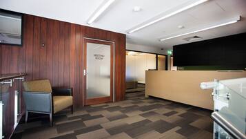 A modern meeting room with a wooden panel wall, a glass door labeled 'MEETING ROOM', a reception desk, and a patterned carpet.