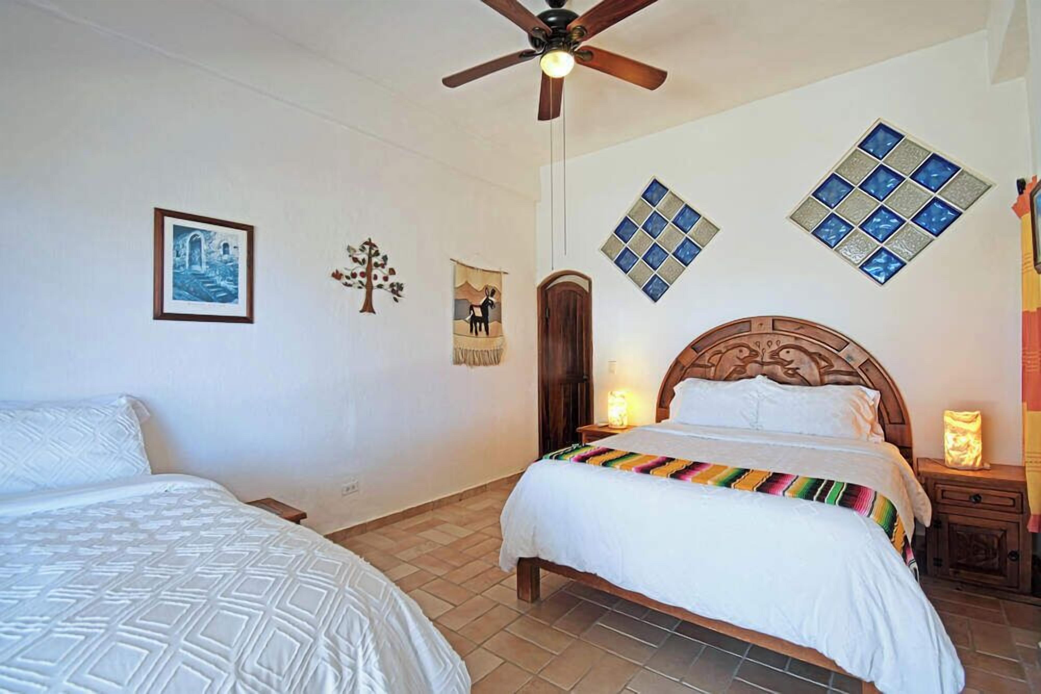 Ein Schlafzimmer mit zwei Betten, einem Holz-Kopfteil, einem Deckenventilator und Wandbildern.