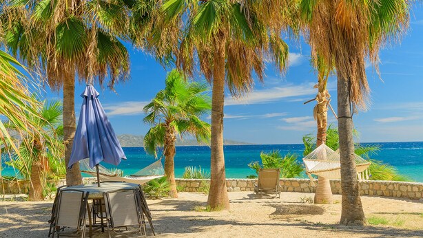 Un paisaje playero con una mesa, sillas, una hamaca y vistas al océano.