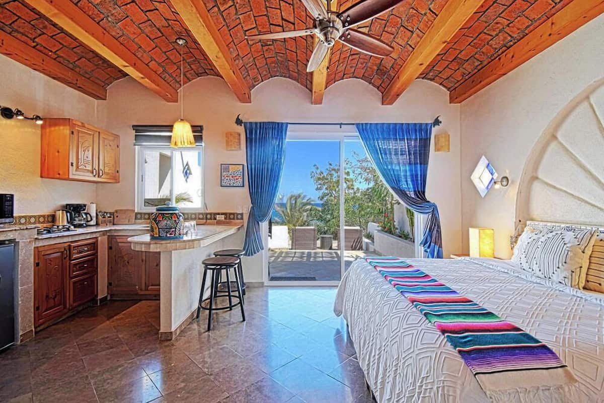A spacious room with a large bed, a kitchen area, and a balcony with a view.
