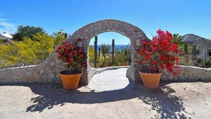Un arco adornado con flores rojas en macetas, un muro de piedra y un cielo azul brillante.