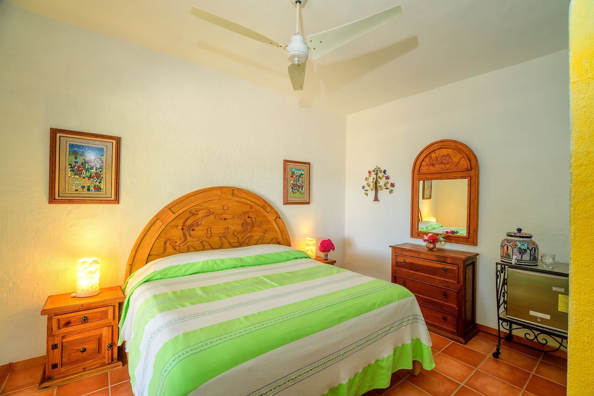 A bedroom with a bed, wooden headboard, bedside table with lamp, dresser, mirror, and ceiling fan.
