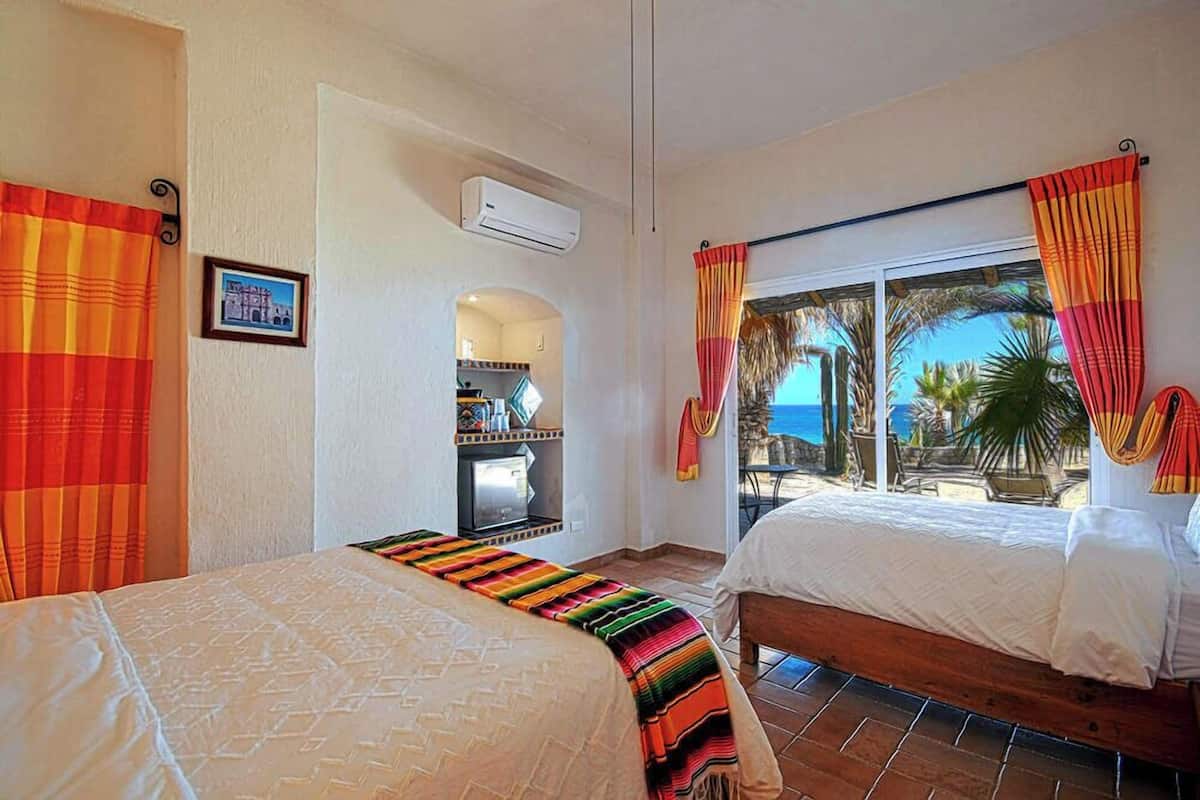 A hotel room with two beds, a kitchenette, and a view of the beach.
