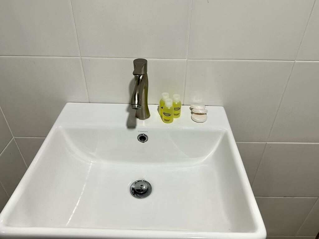 A white bathroom sink with a single faucet and three bottles of hand soap on the counter.
