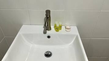 A white bathroom sink with a single faucet and three bottles of hand soap on the counter.