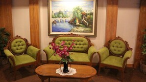 A room with three green upholstered chairs, a wooden coffee table with a vase of flowers, and a framed painting of a riverside scene on the wall. - Hotel Regal Malaysia (George Town)