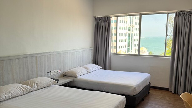 A hotel room with two beds, a chair, a window with a view of buildings and the sea, and a ceiling vent. - Hotel Regal Malaysia (George Town)