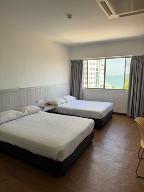 A hotel room with two beds, a chair, a window with a view of buildings and the sea, and a ceiling vent. - Hotel Regal Malaysia (George Town)