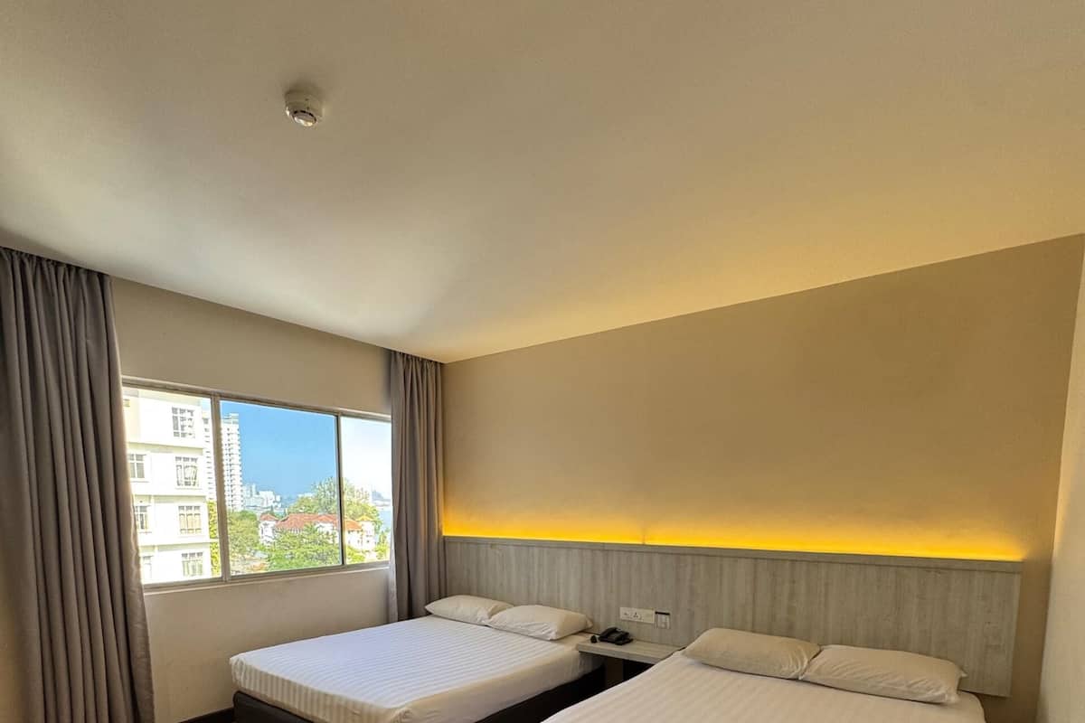 Una habitación de hotel con dos camas, un ventanal con cortinas y vistas a edificios.