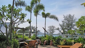 Un patio con mobiliario de madera, cerca blanca y plantas tropicales.