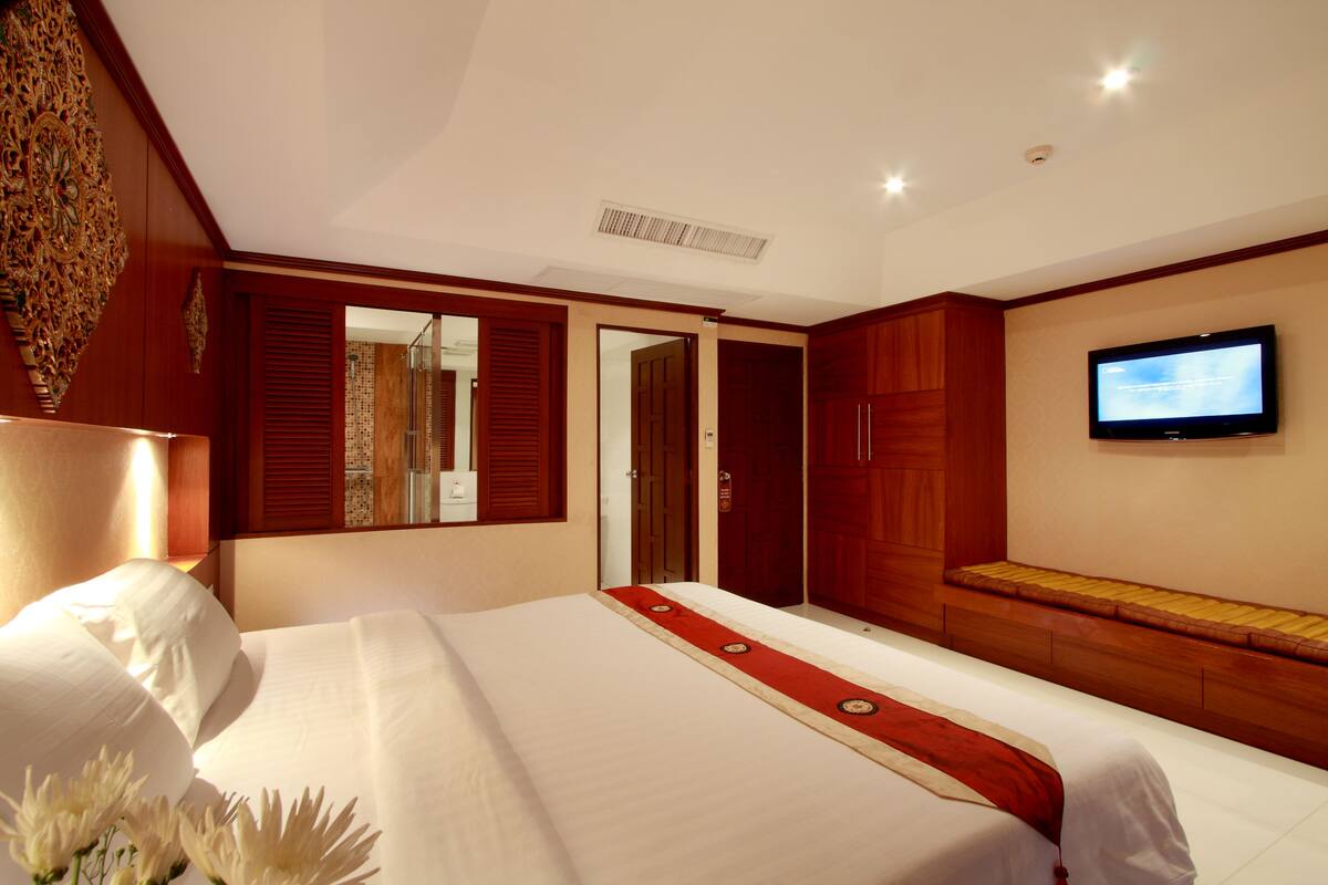 A hotel room with a large bed, a television mounted on the wall, and a wooden bench along the wall.