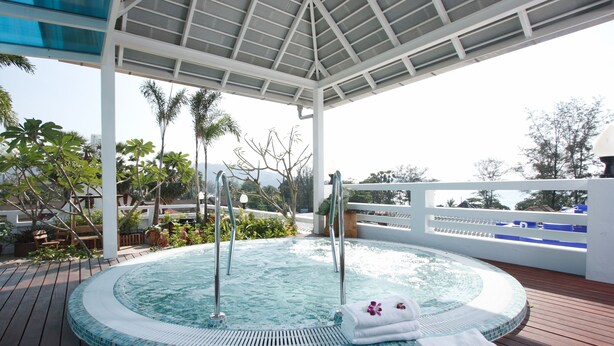 Un jacuzzi bajo un área techada con una terraza de madera, rodeado de plantas tropicales y vistas al mar.