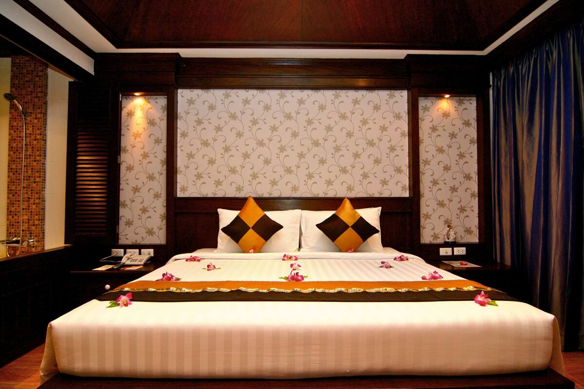 A hotel room with a large bed, two nightstands, a wooden headboard, and patterned wallpaper.