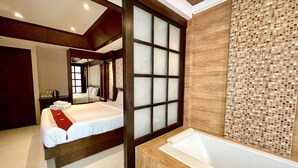 Una habitación de hotel moderna con una cama grande, un baño separado con bañera y una puerta de vidrio corredera.