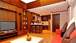 Una sala de estar con televisor, una mesa de centro con un florero, un sofá rojo y armarios de madera.