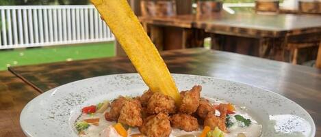 A plate of food with fried items and vegetables on a table in a restaurant with a view of greenery outside.