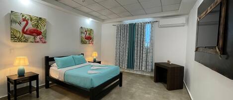 Quarto com cama, duas mesas de cabeceira, um criado-mudo, janela com cortinas e decoração na parede.
