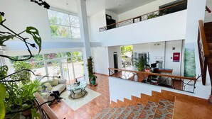 A spacious, modern interior with a high ceiling, a staircase leading to an upper level, and a view of the outdoors through large windows. - Hotel Coronado Inn (Las Lajas)