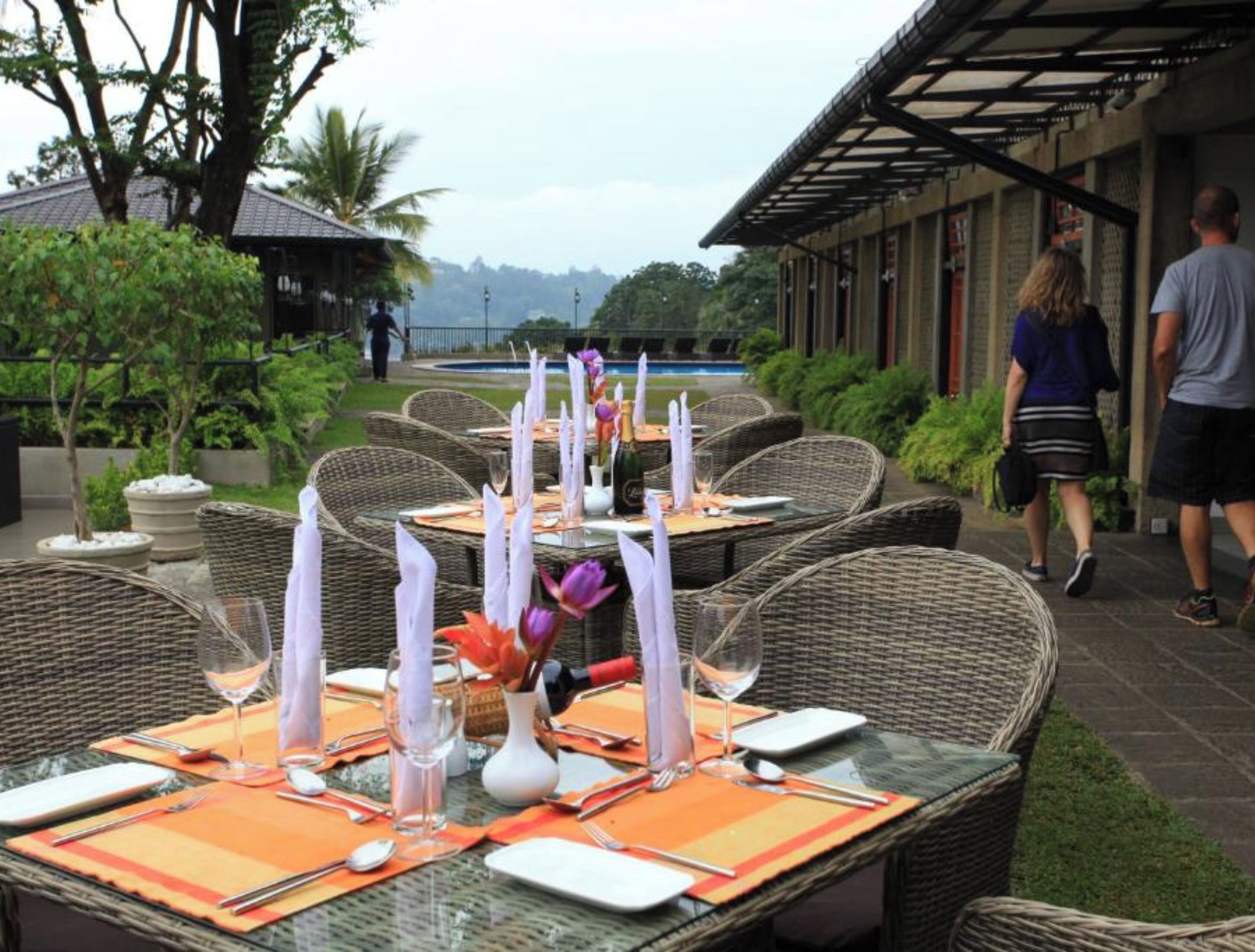 An outdoor dining area with wicker tables, orange placemats, and candles.