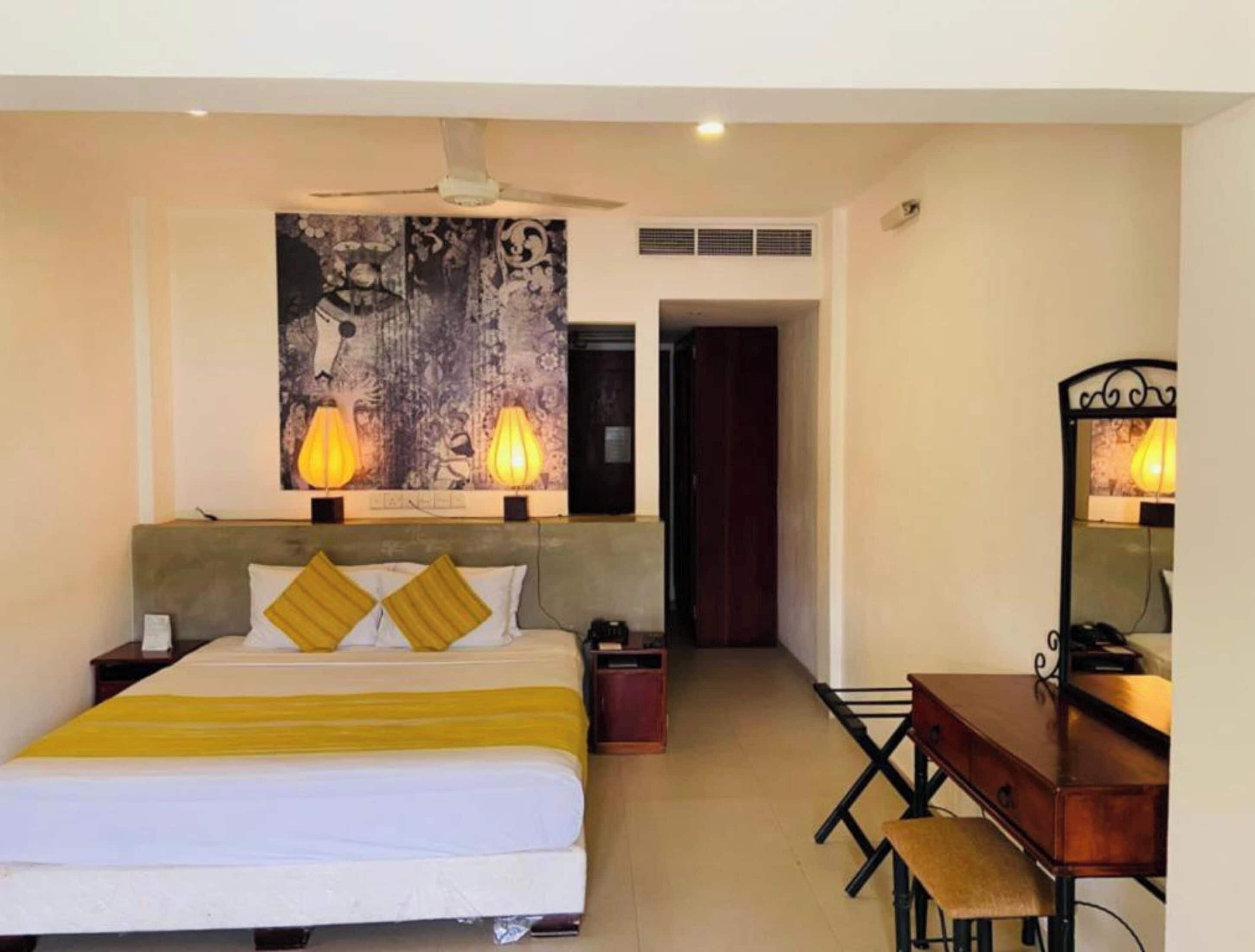 Una habitación de hotel con cama, mesita de noche, escritorio, silla y un espejo grande.