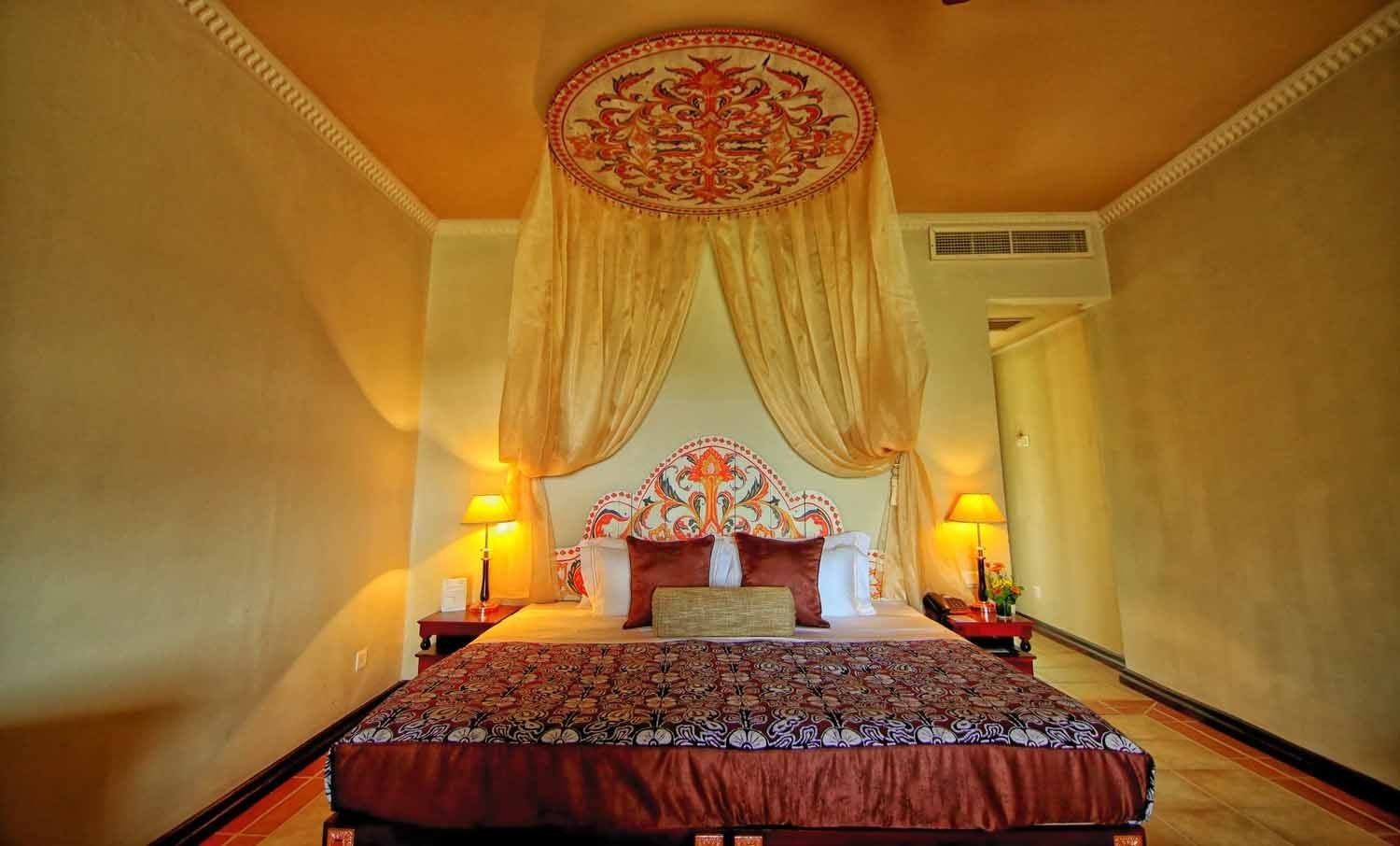 A hotel room with a large bed, ornate headboard, and two bedside lamps.