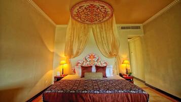 A hotel room with a large bed, ornate headboard, and two bedside lamps.