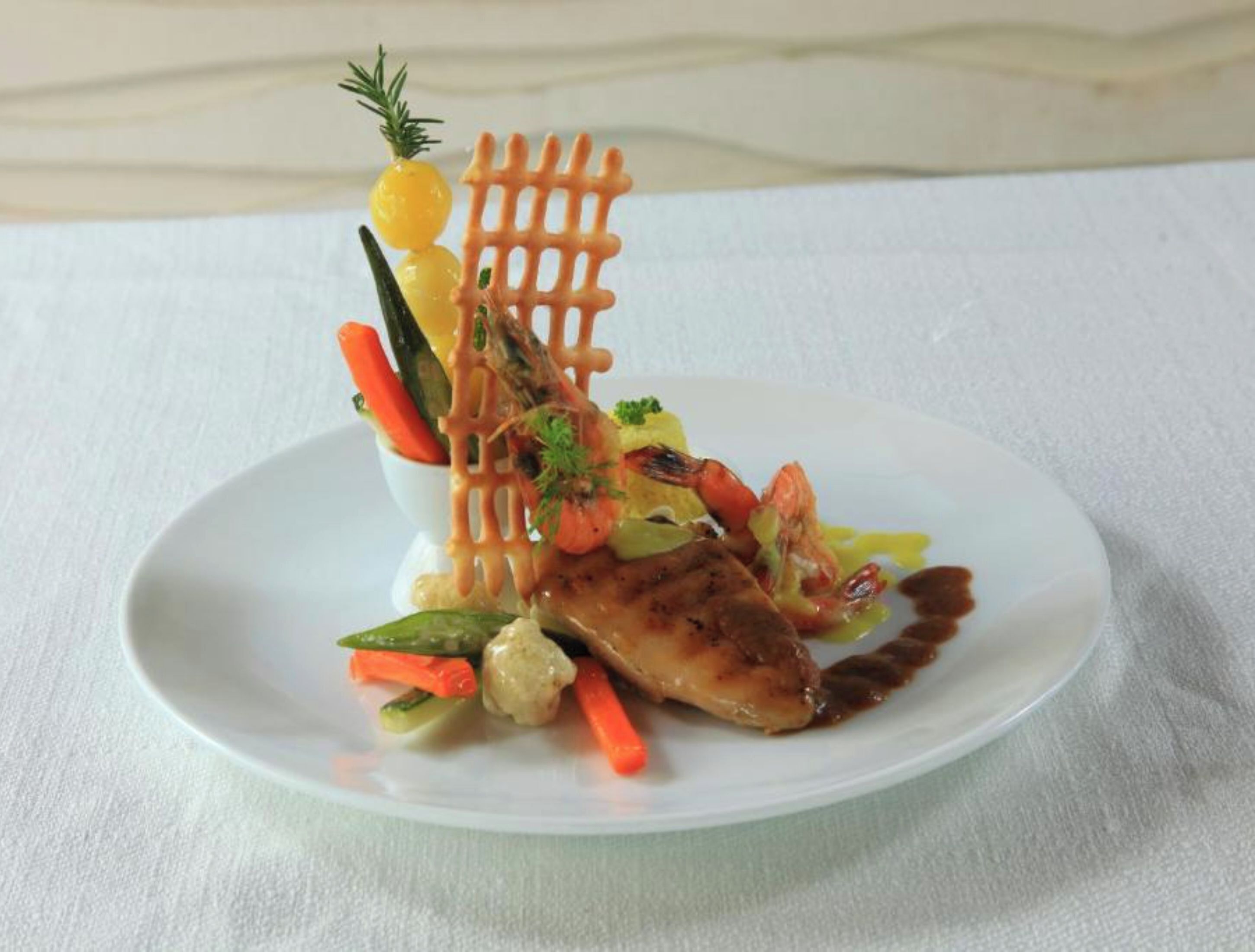Une assiette blanche contenant un morceau de poisson grillé, des légumes et un élément décoratif.