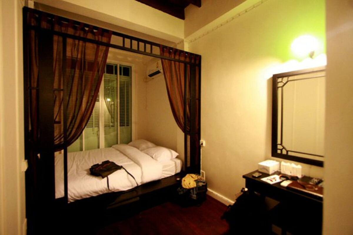 Un lit simple avec un baldaquin, une table de chevet avec une lampe et un miroir au mur.