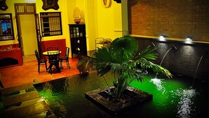 Een kamer met een eettafel, stoelen, een klein waterpartij en een bakstenen muur.