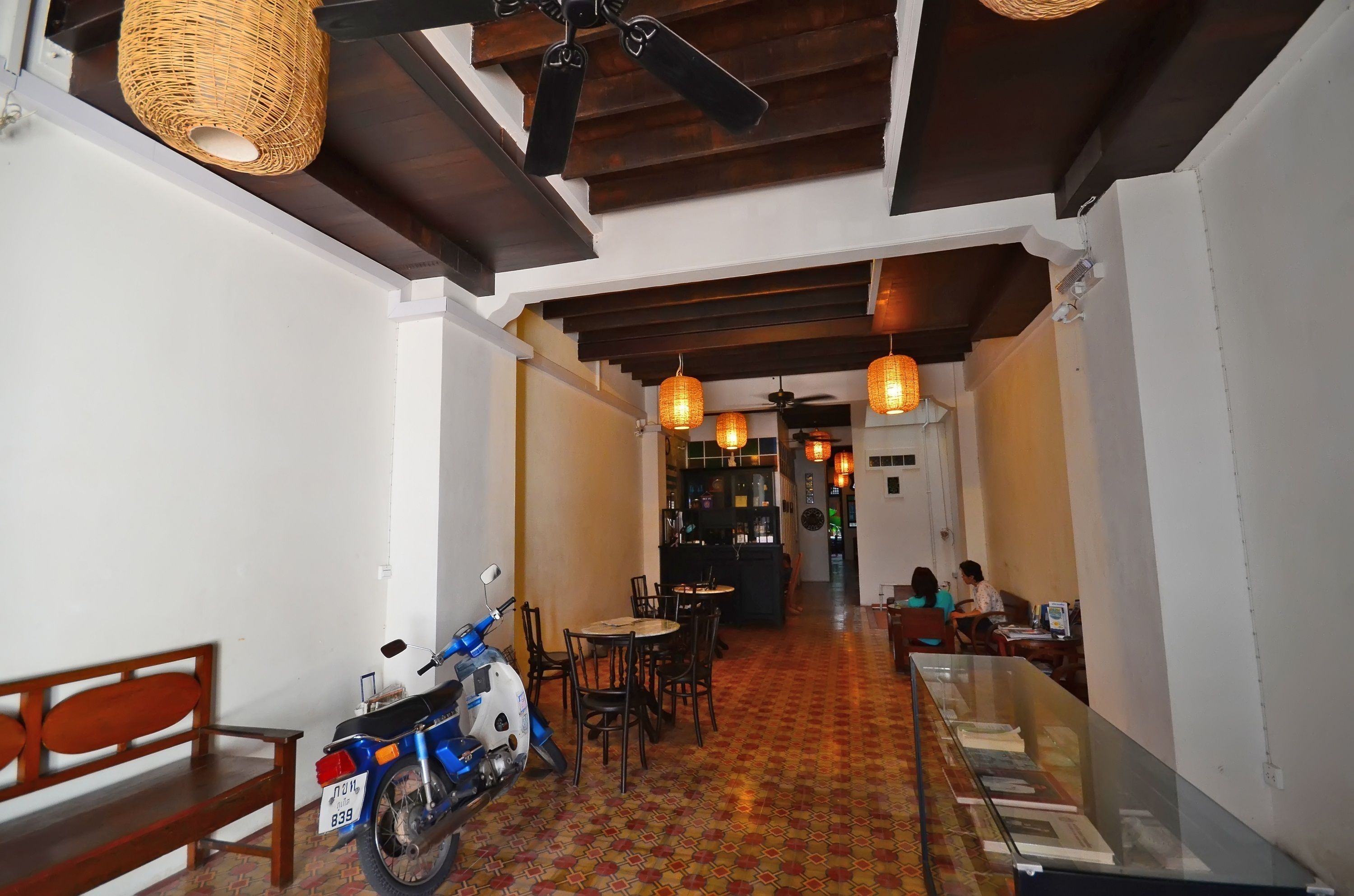 A hallway with a patterned floor, wooden benches, a scooter, and tables with chairs.
