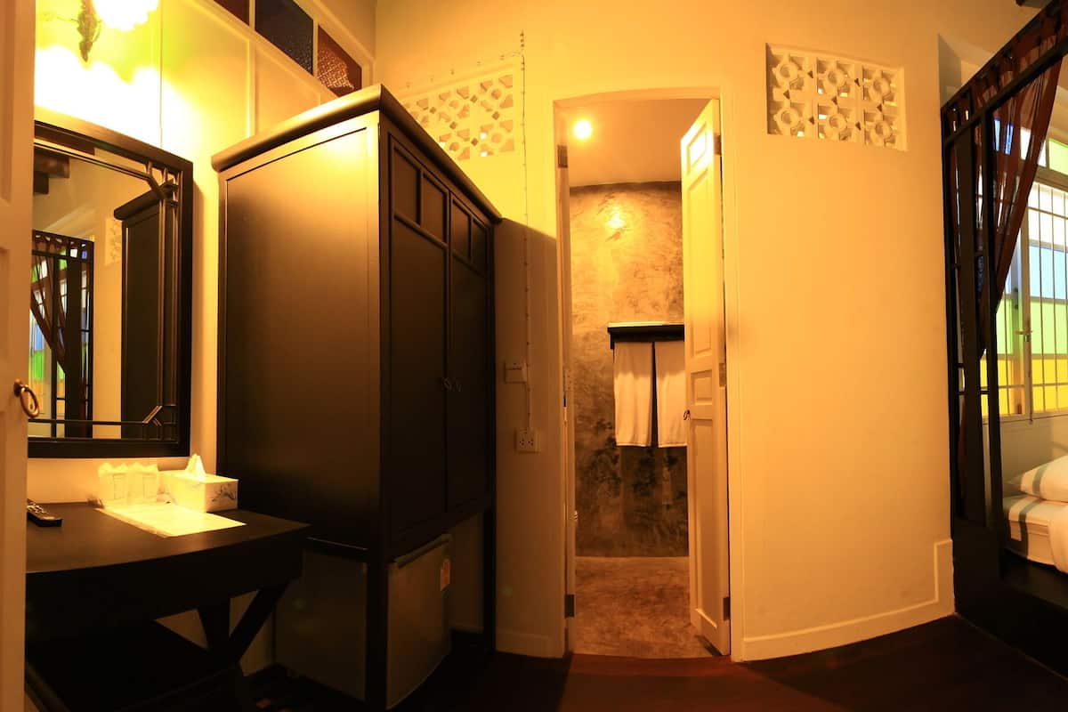 Une chambre à coucher avec un lit, un bureau et un miroir. On peut apercevoir une salle de bain à travers une porte ouverte.