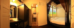 A bedroom with a bed, a desk, and a mirror. There is a bathroom visible through an open door. - 99 OLDTOWN BOUTIQUE GUESTHOUSE (Phuket)