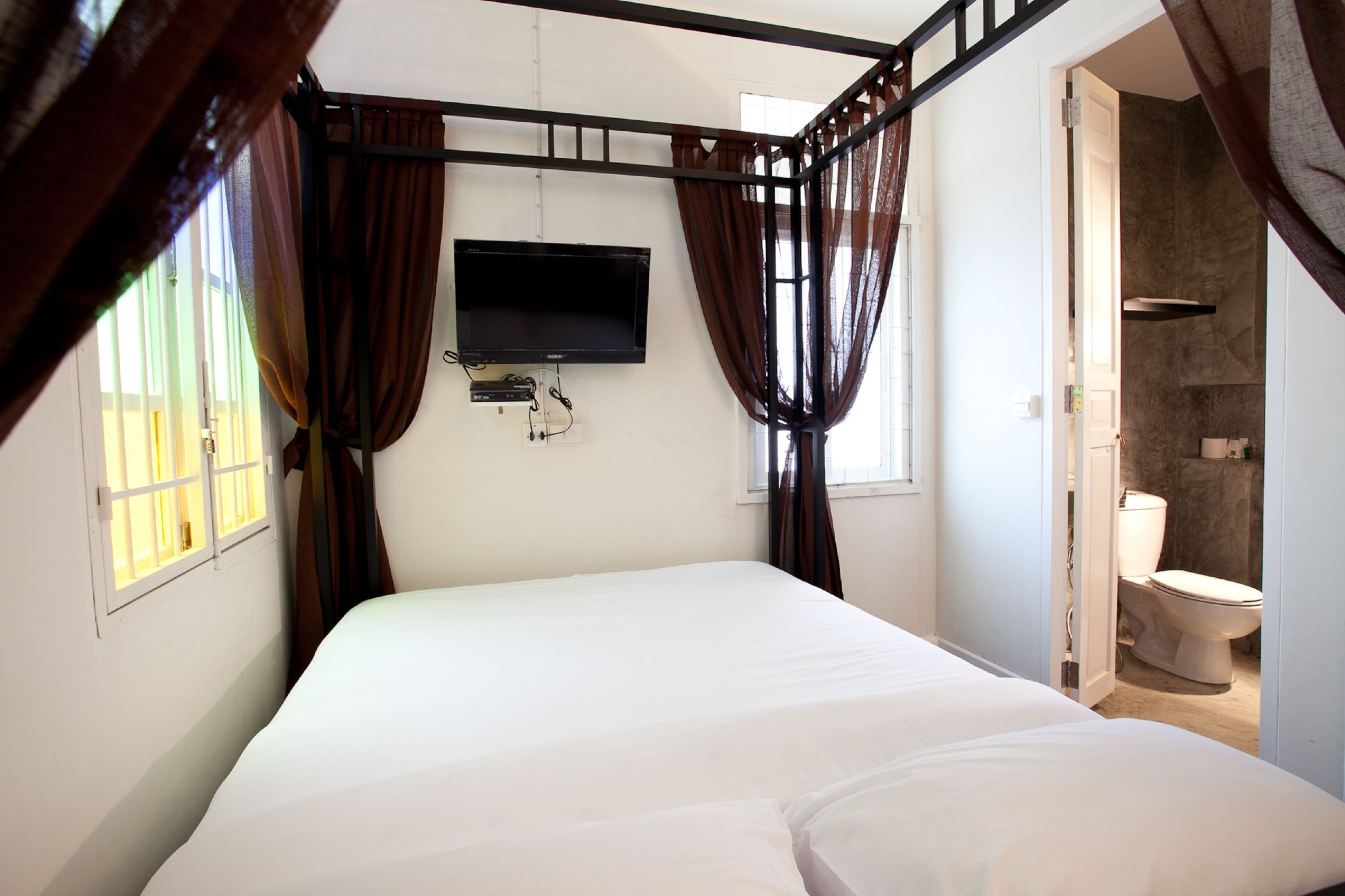 A bedroom with a bed, a television mounted on the wall, and a bathroom visible through an open door.