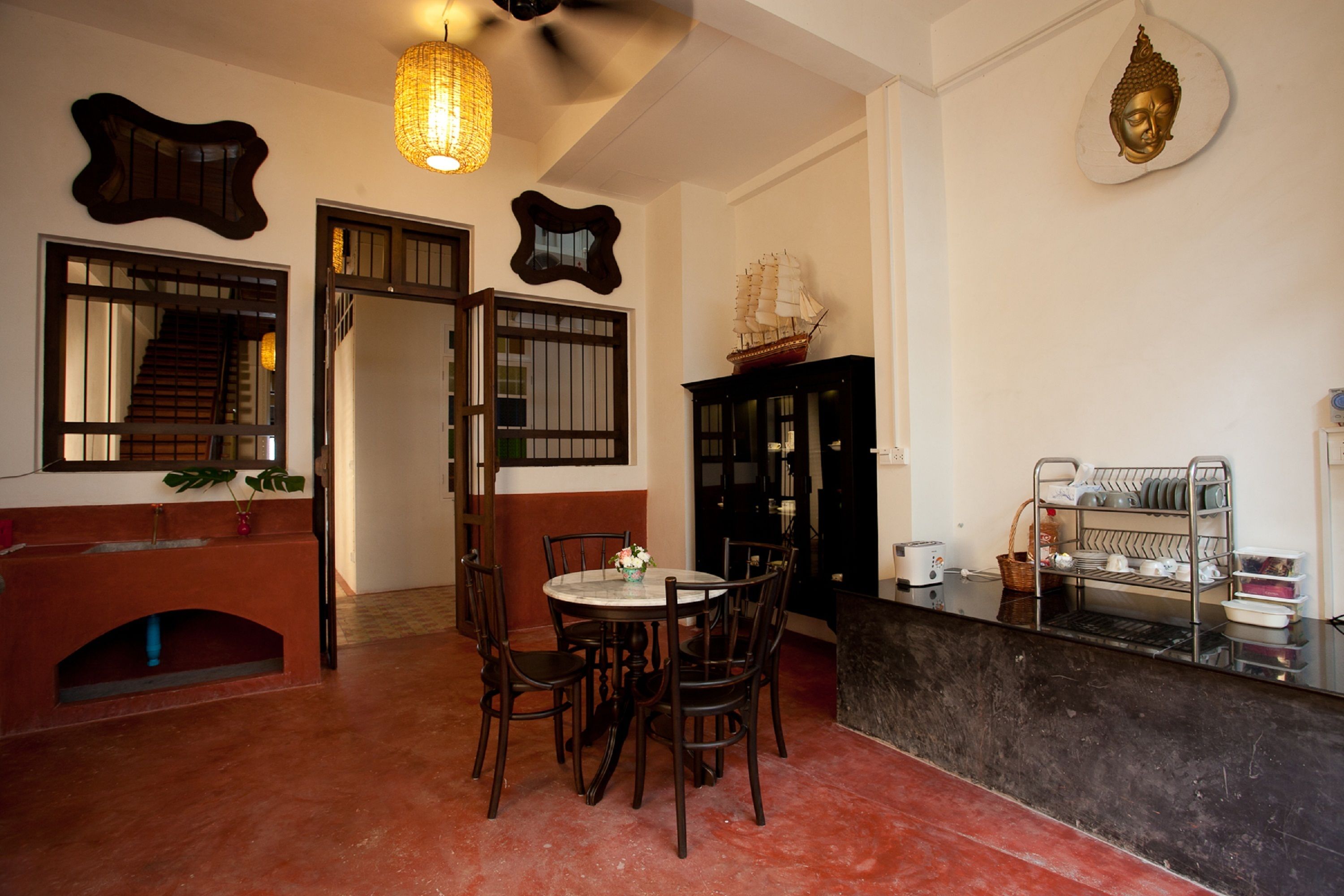 A dining area with a round table, chairs, a ship model, and a Buddha head decoration.