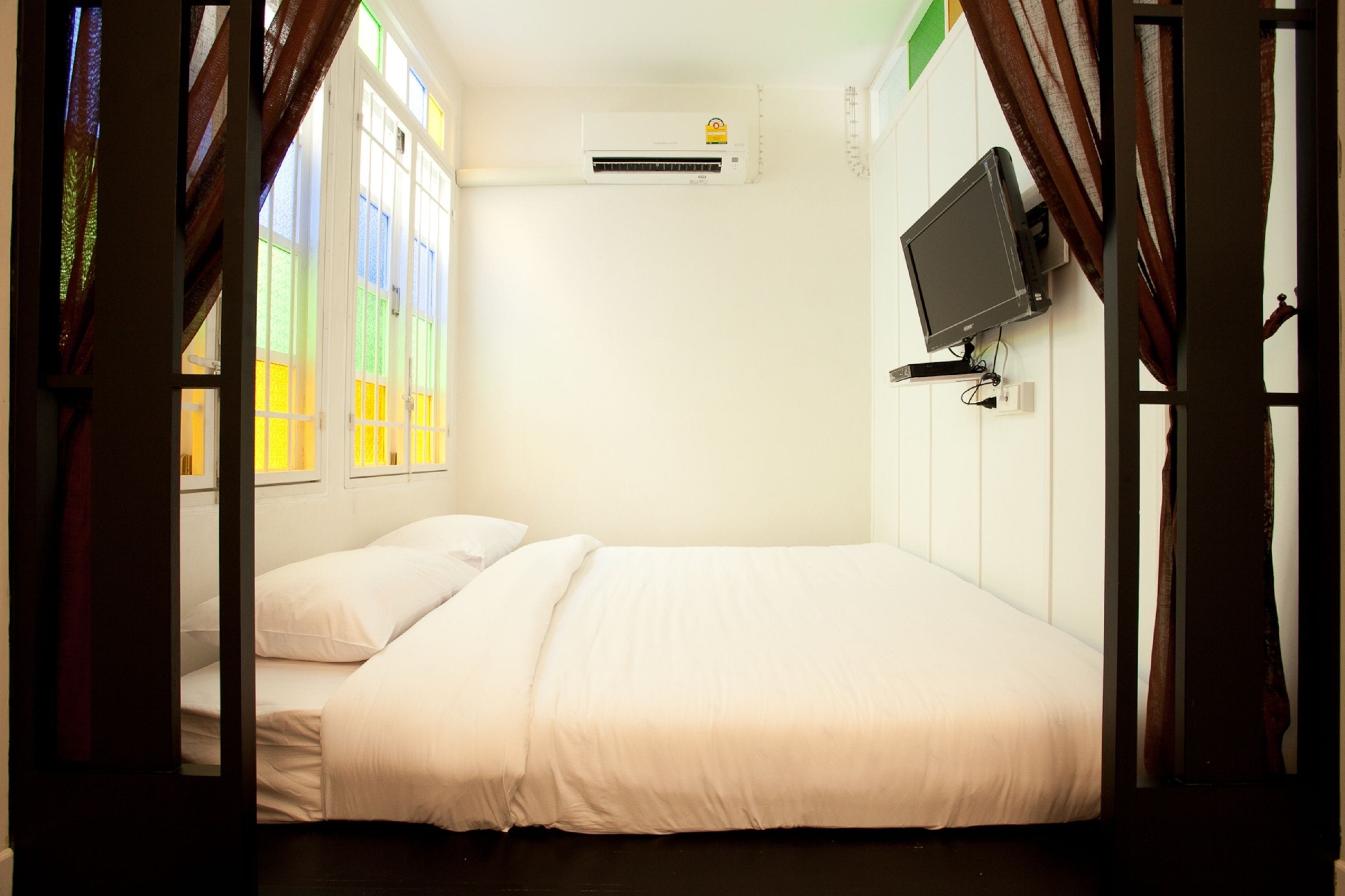 A single bed with white bedding, a mounted TV, and an air conditioning unit on the wall.