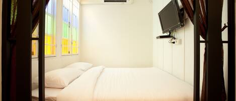 A single bed with white bedding, a mounted TV, and an air conditioning unit on the wall.