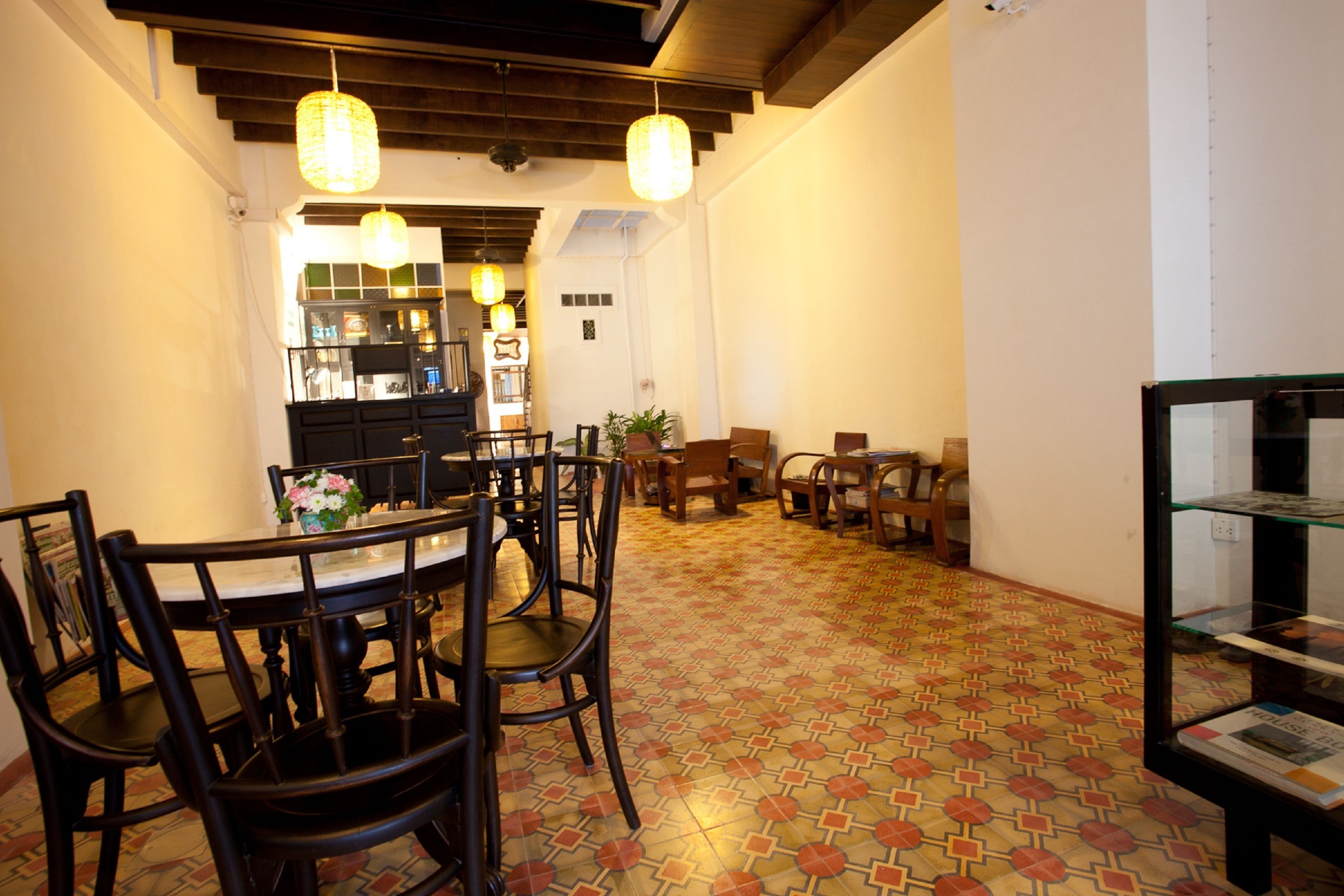 A dining area with a patterned floor, wooden chairs, a table with a vase of flowers, and hanging lights.