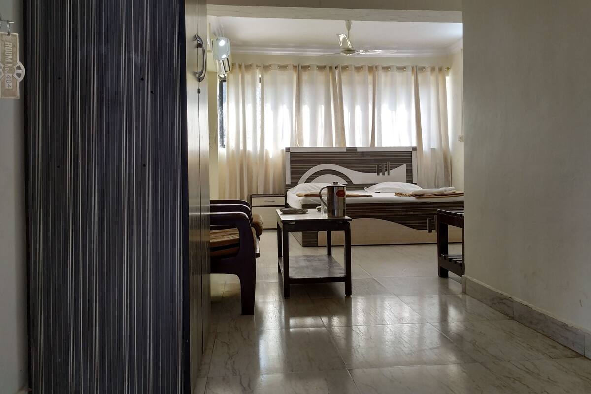Una habitación de hotel con cama, escritorio, silla, cafetera y ventana con cortinas.