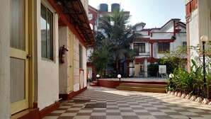 A corridor with a checkered floor, a fire extinguisher, and a building entrance with a sign. - Atlanta Beach Resort (Calangute)