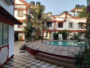 A courtyard with a swimming pool, steps leading to the pool, and a building with multiple balconies. - Atlanta Beach Resort (Calangute)