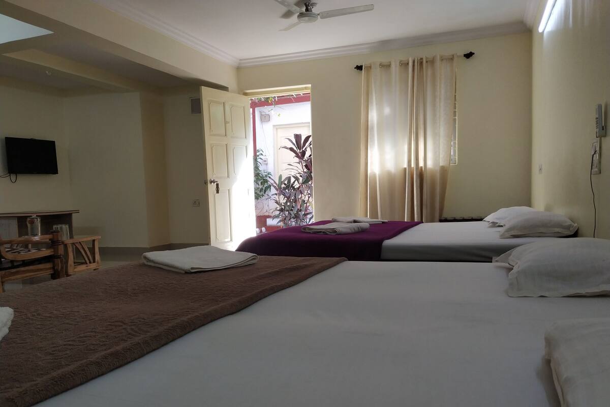 Habitación de hotel con dos camas, televisor, escritorio y ventana con cortinas.