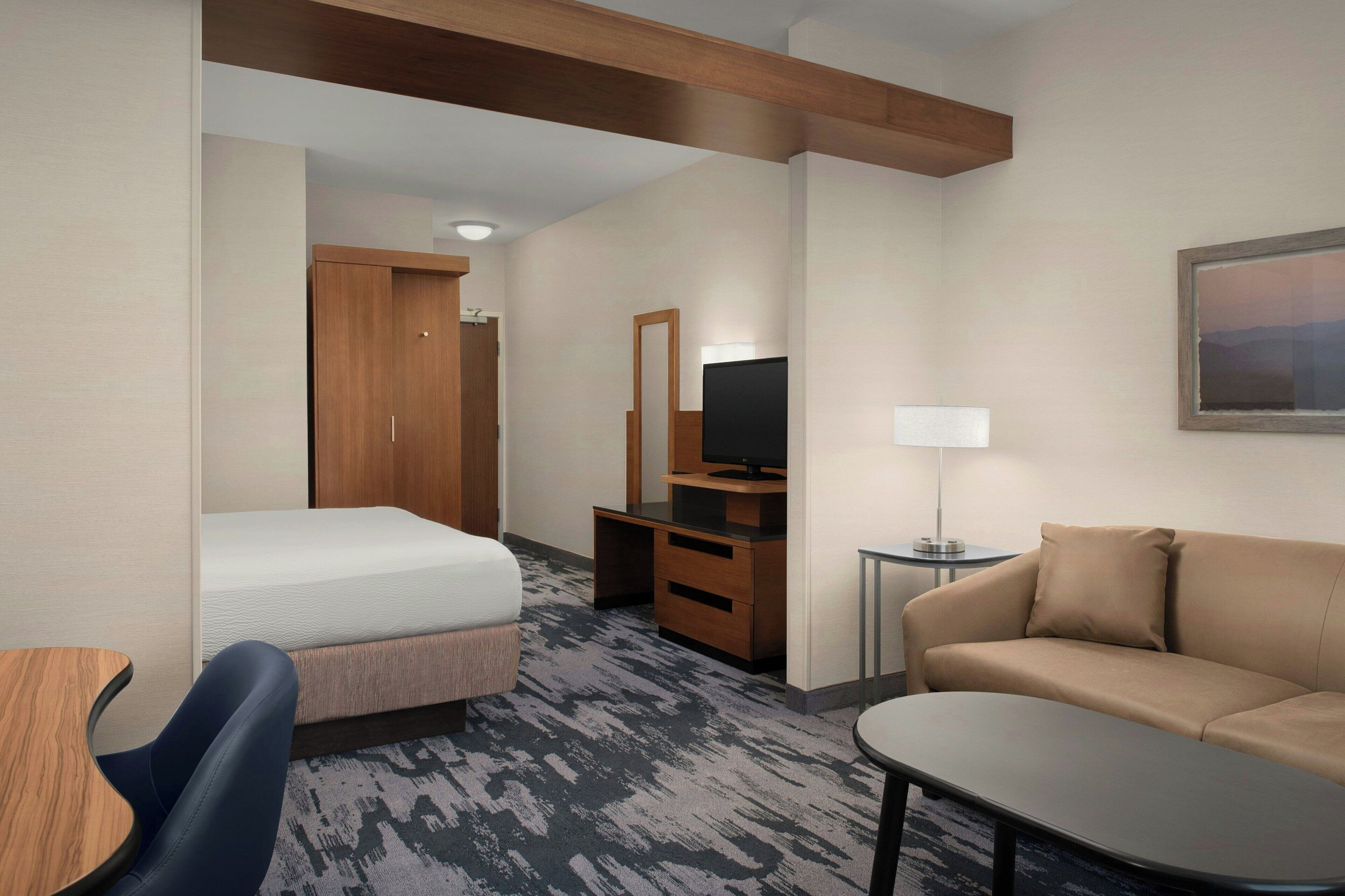 A hotel room with a bed, a desk with a TV, a sofa, and a small table.