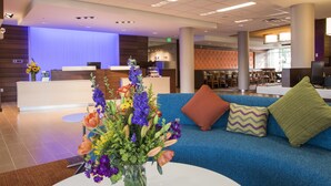 Un hall d’hôtel avec un comptoir d’accueil, un canapé bleu agrémenté de coussins décoratifs et un arrangement floral posé sur une table.