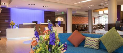 Eine Hotelhalle mit einer Rezeption, einem blauen Sofa mit Zierkissen und einer Blumenkomposition auf einem Tisch.