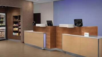 A hotel reception area with wooden reception desks, a refrigerated display case, and a blue wall.